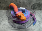 a purple and orange toy snake sitting on top of a spool of purple wire