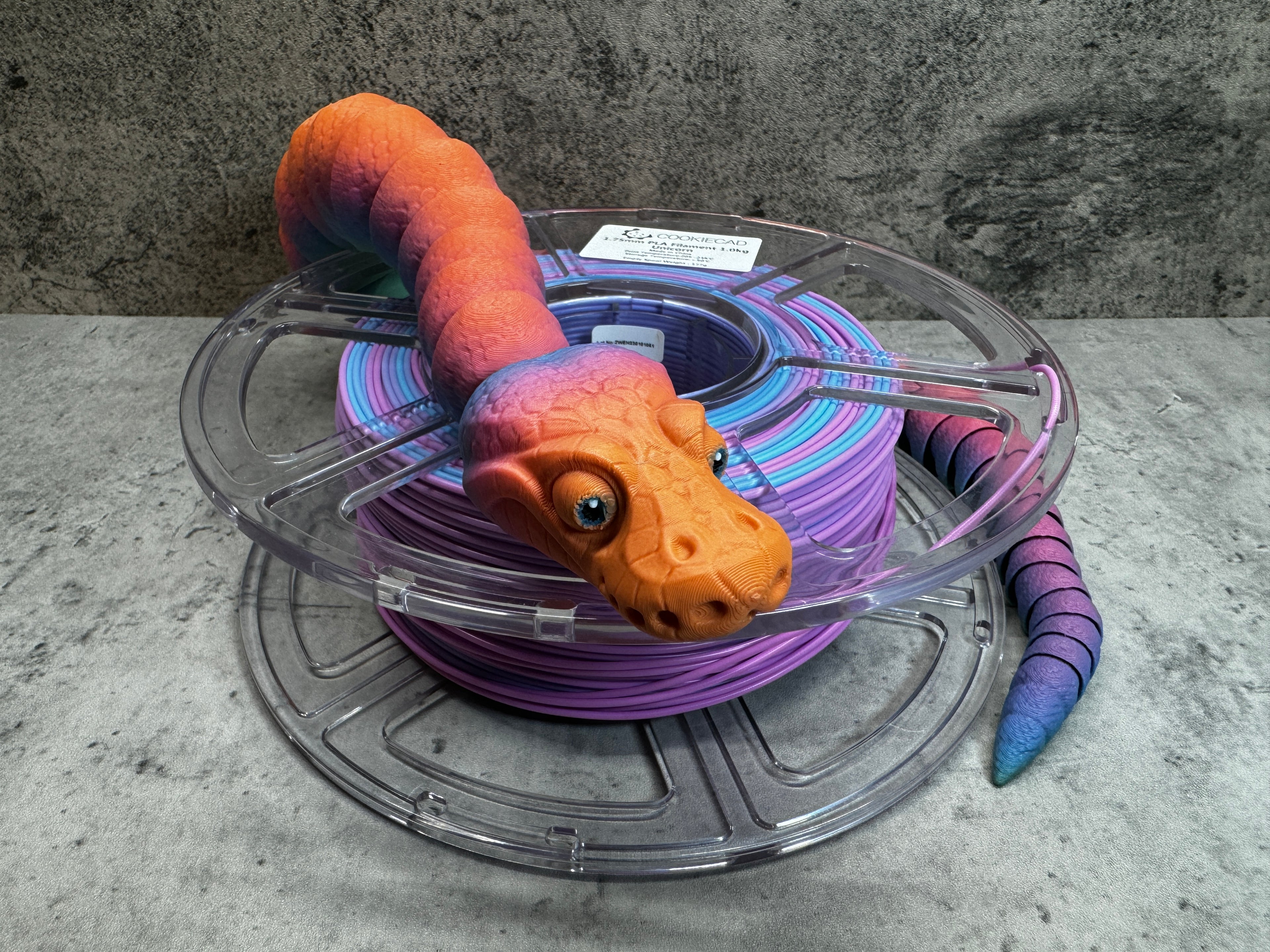 a purple and orange toy snake sitting on top of a spool of purple wire
