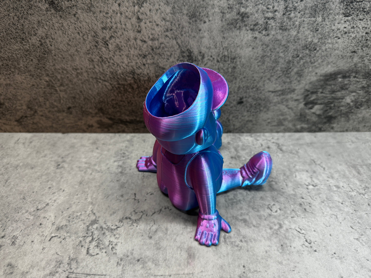 
                  
                    a purple and blue toy sitting on top of a cement floor
                  
                