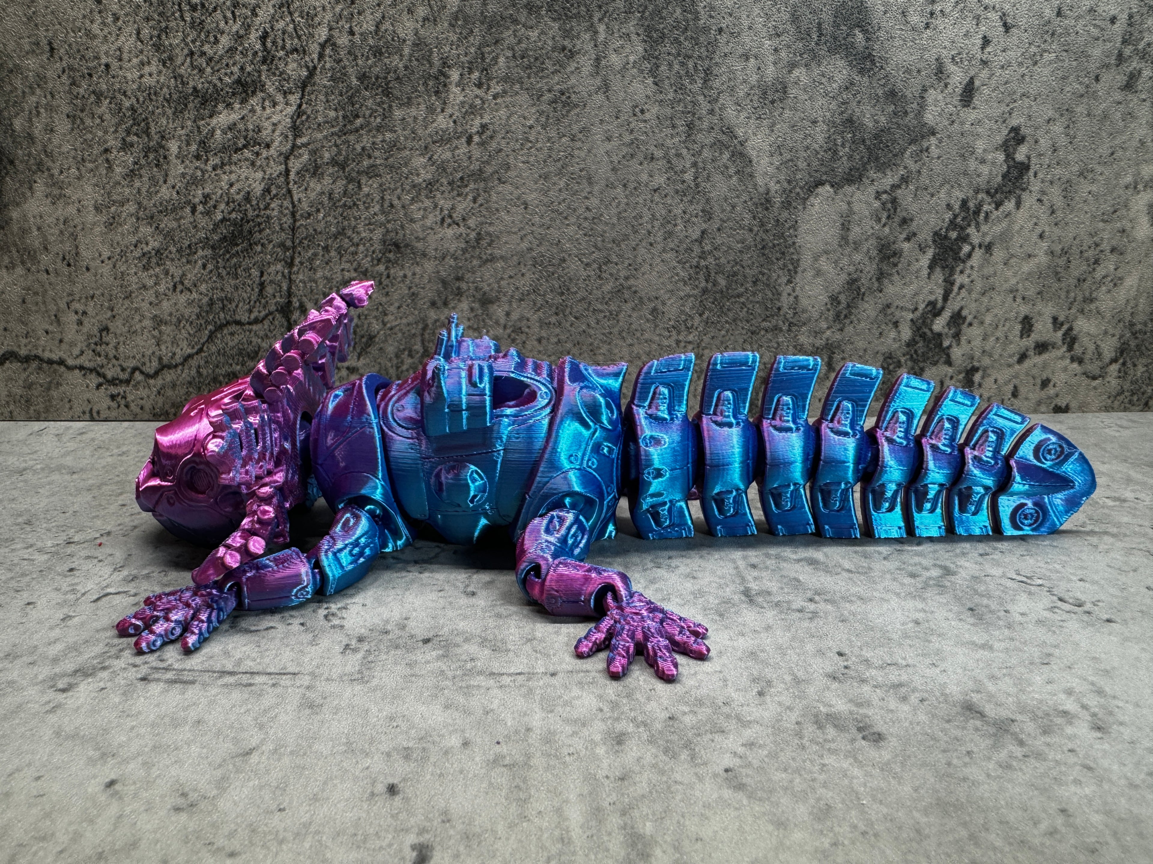 a purple and blue toy lizard laying on the ground