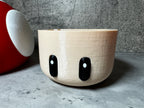 a white bowl with black eyes sitting next to a red vase