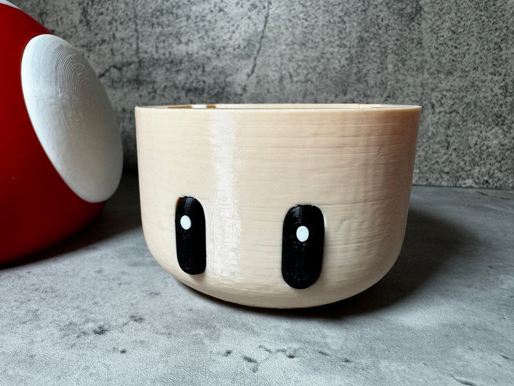 
                  
                    a white bowl with black eyes sitting next to a red vase
                  
                