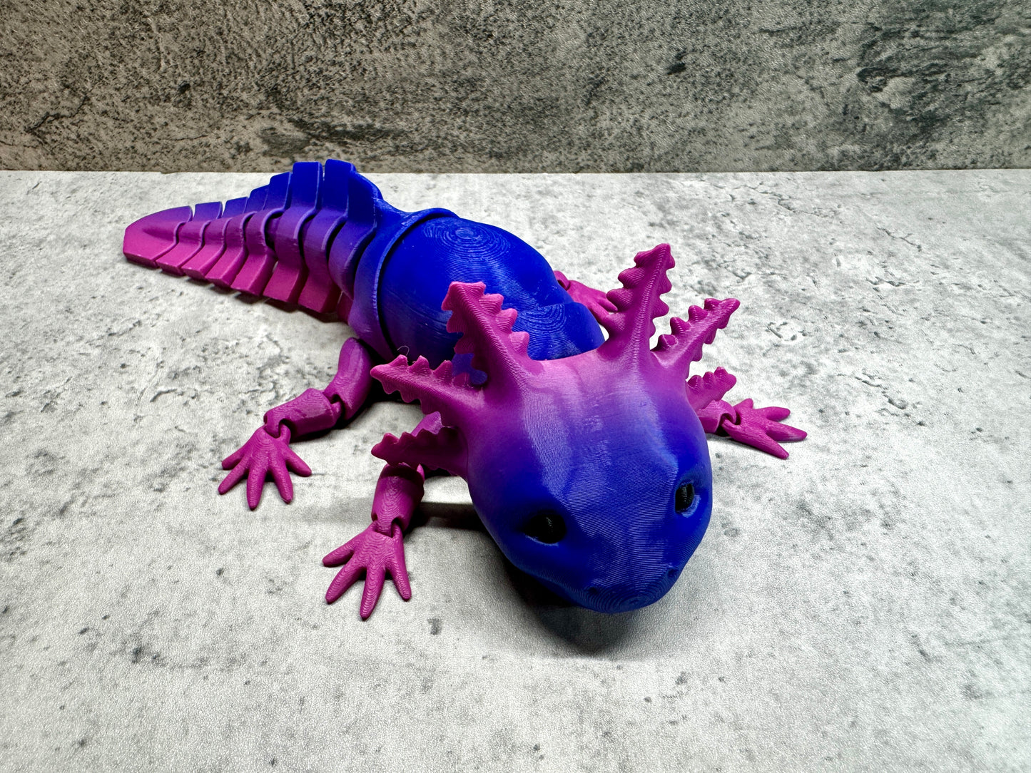 a purple and blue toy lizard laying on a white surface